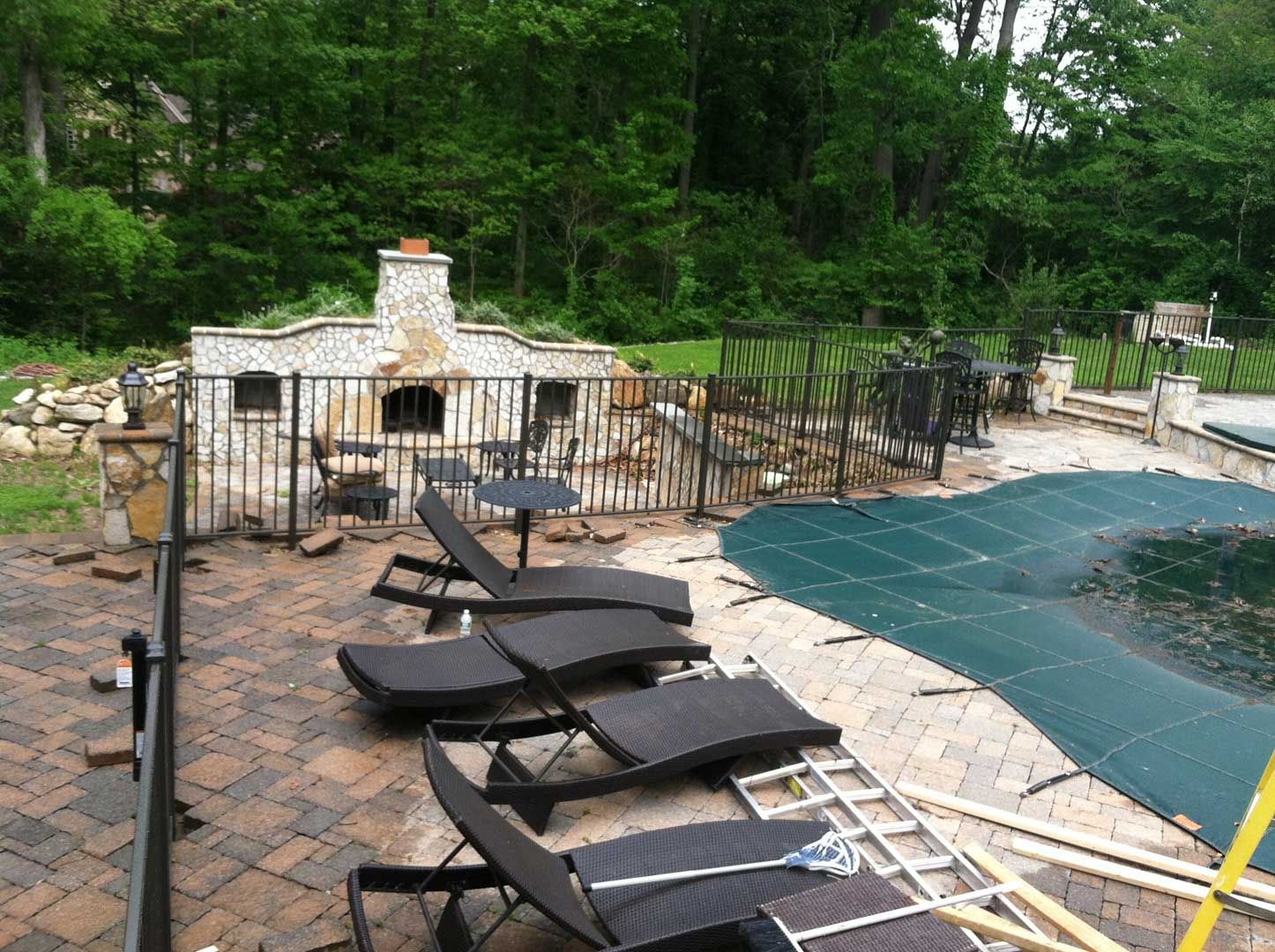 Outdoor pizza oven and pool area with lounge chairs and foliage.