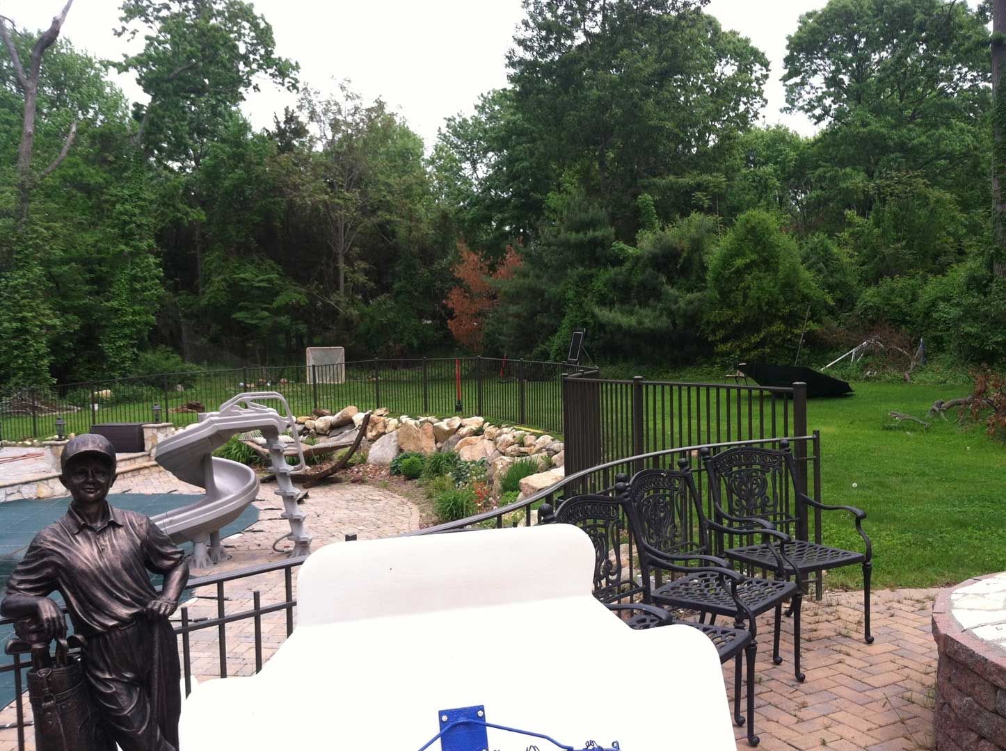 Backyard with pool, sculpture, seating, and pond surrounded by trees on a cloudy day.