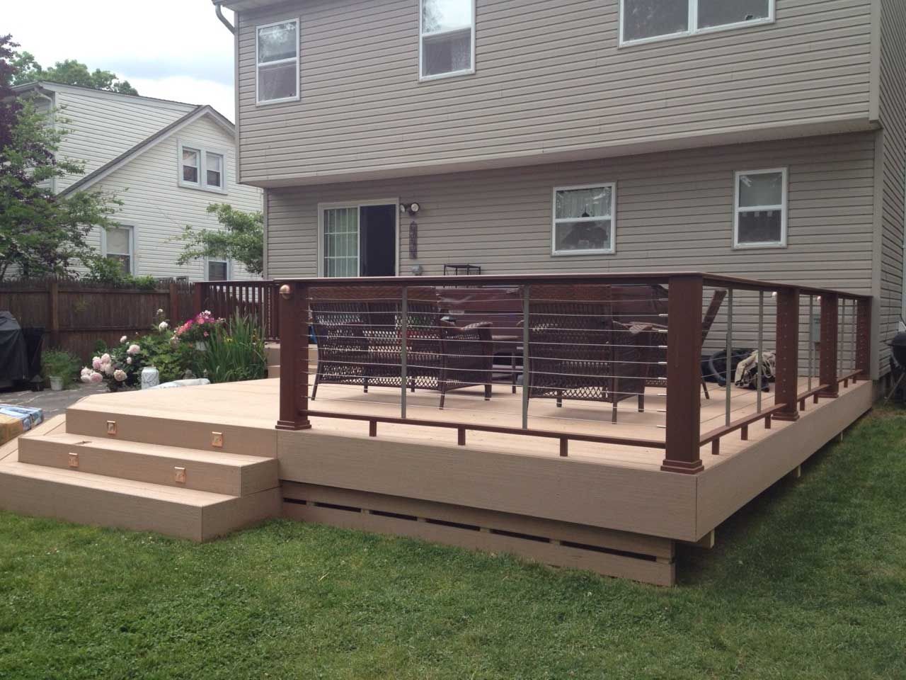 Backyard deck with brown railing, steps, and tan composite boards; lawn, house in background.