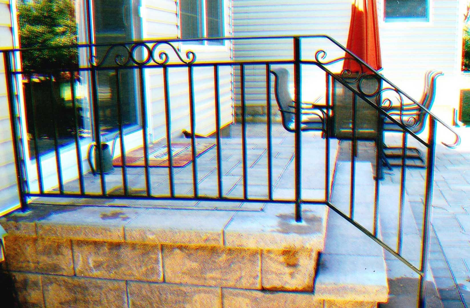 Black wrought iron railing on stone steps leading to a patio with outdoor seating.