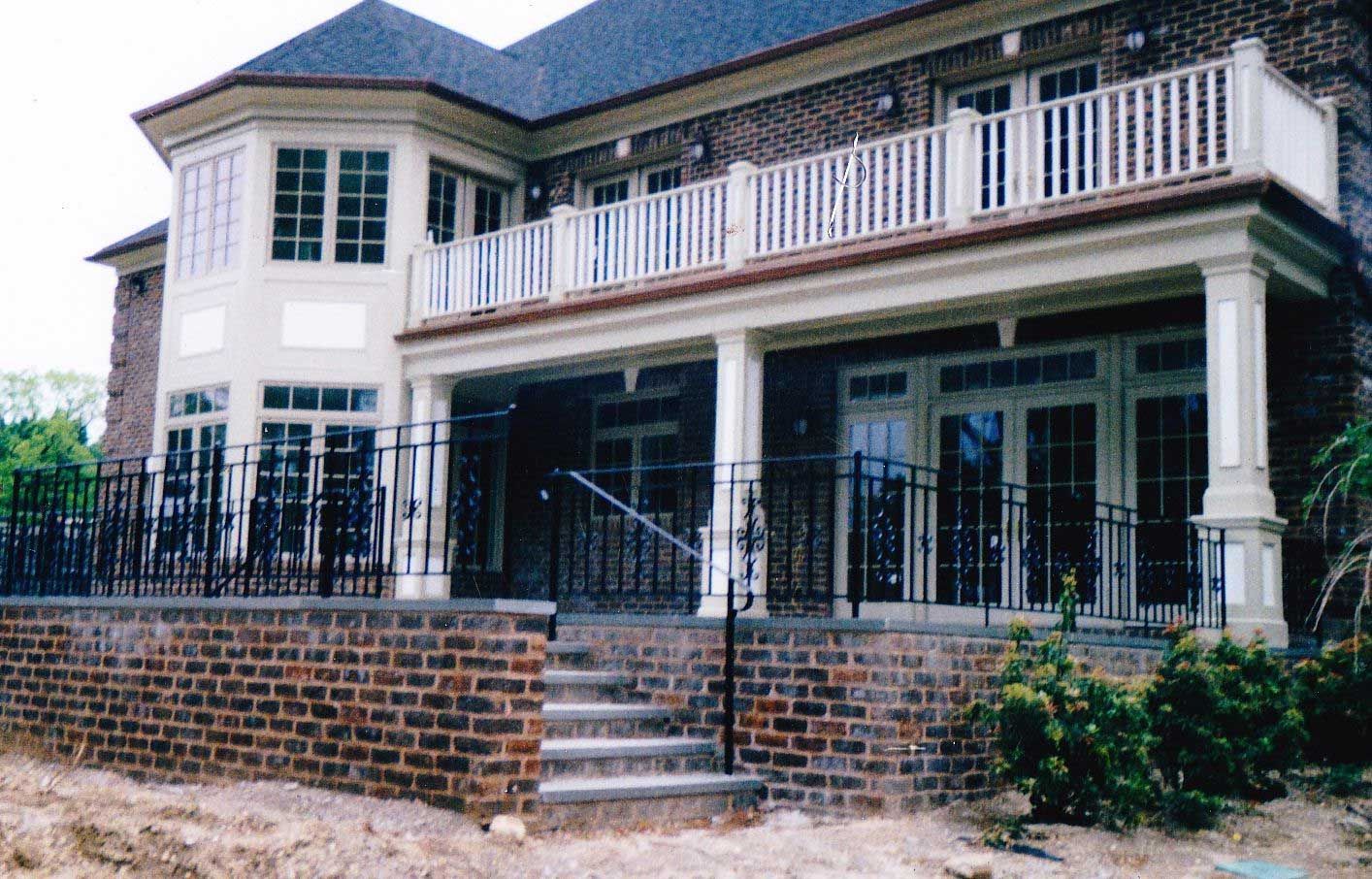 Two-story brick house with a balcony and a lower patio with steps and wrought iron railing.