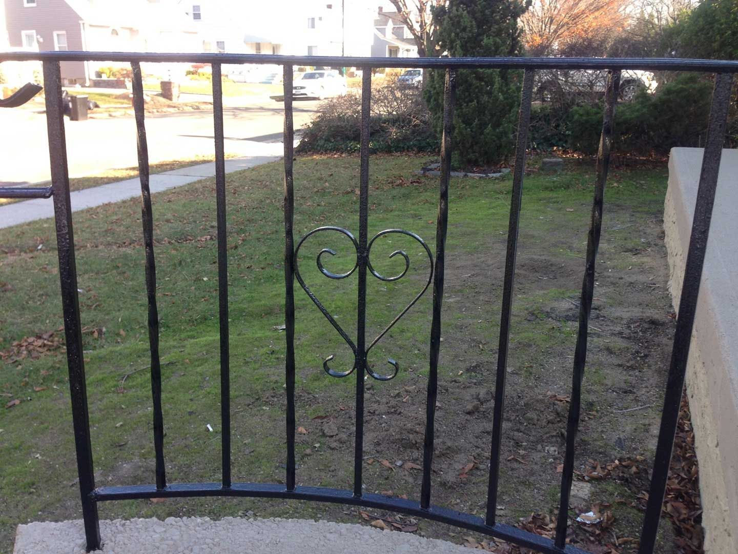 Black metal fence with a heart design in a grassy yard.
