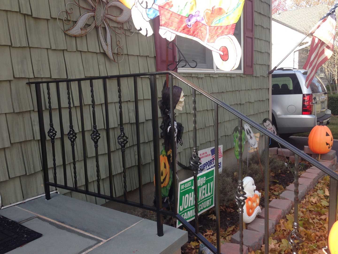 Halloween decorations on a porch, including a skeleton, pumpkin, and sign, near a black metal railing.