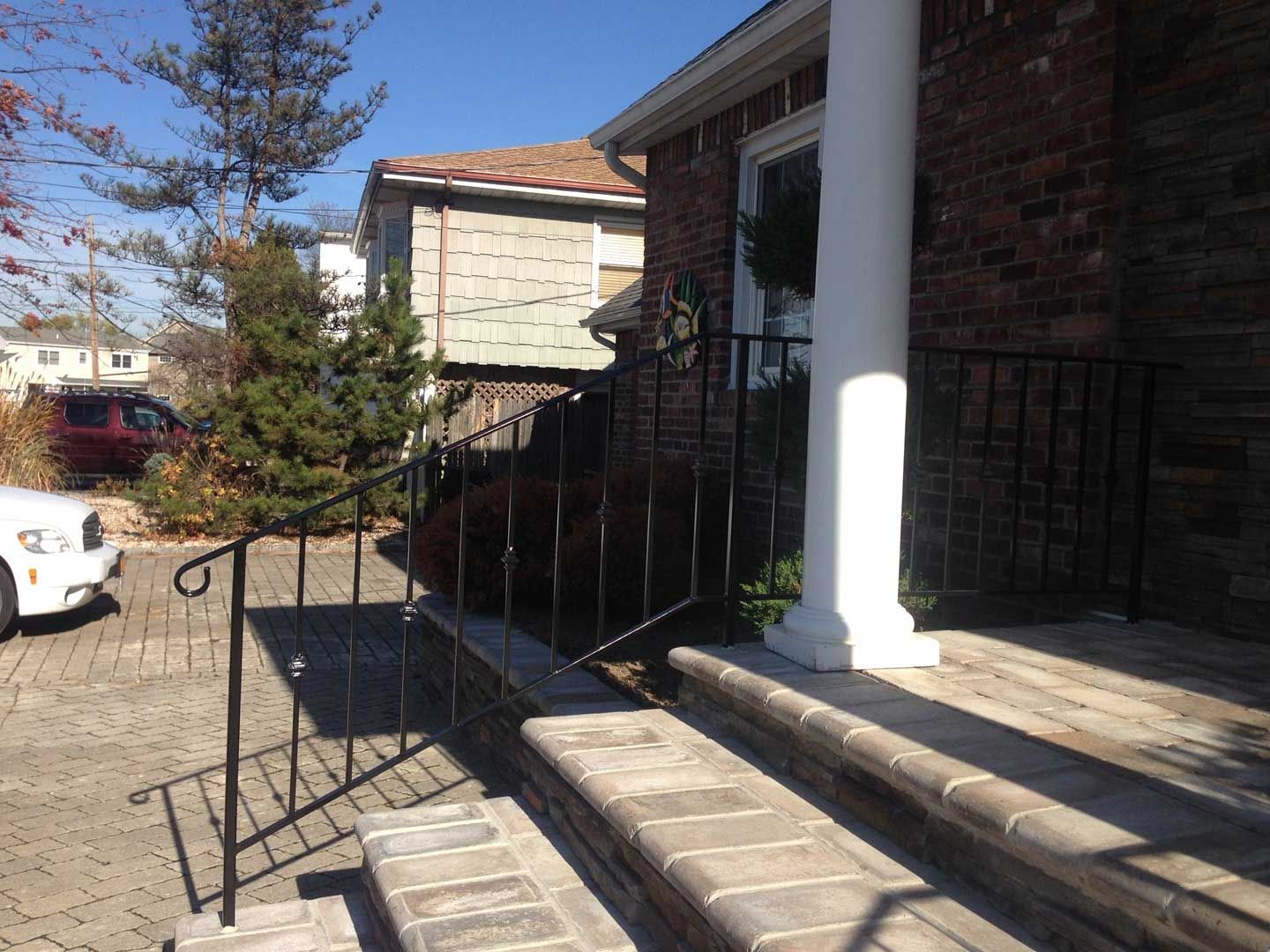 Brick house entrance with steps and ramp; black iron railing; white column; light exterior.