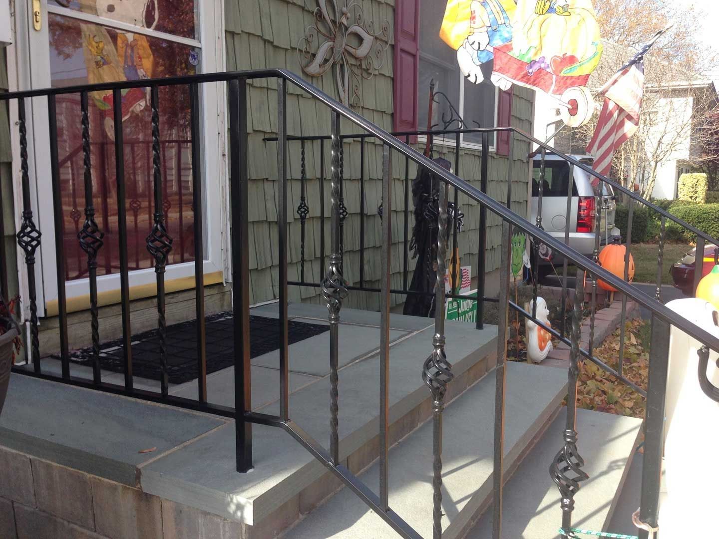 Black wrought iron railing on a porch with stone steps, a front door, and decorations.