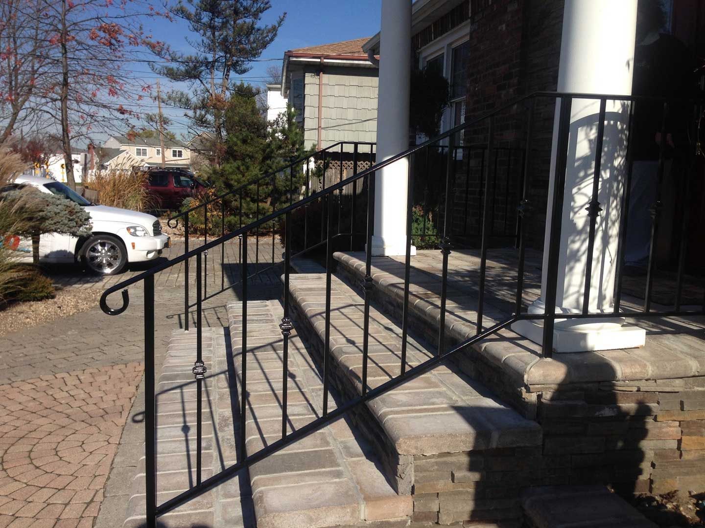 Black metal railing on stone steps leading up to a house with a white column.