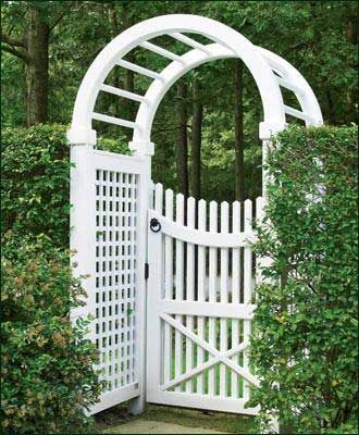 White wooden garden gate with arched trellis, framed by hedges, in a green outdoor setting.
