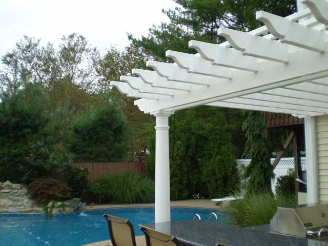 White pergola over a blue swimming pool, with greenery in the background.