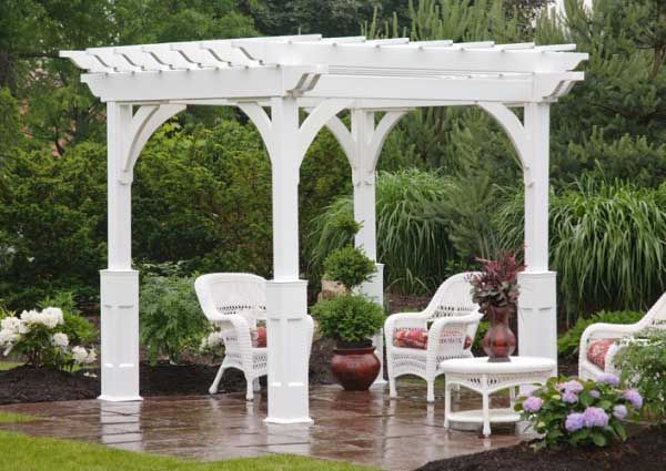 White pergola with arched supports over a patio with white wicker furniture and potted plants.
