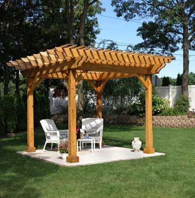 Wooden pergola with chairs and a small table on a concrete patio in a yard.