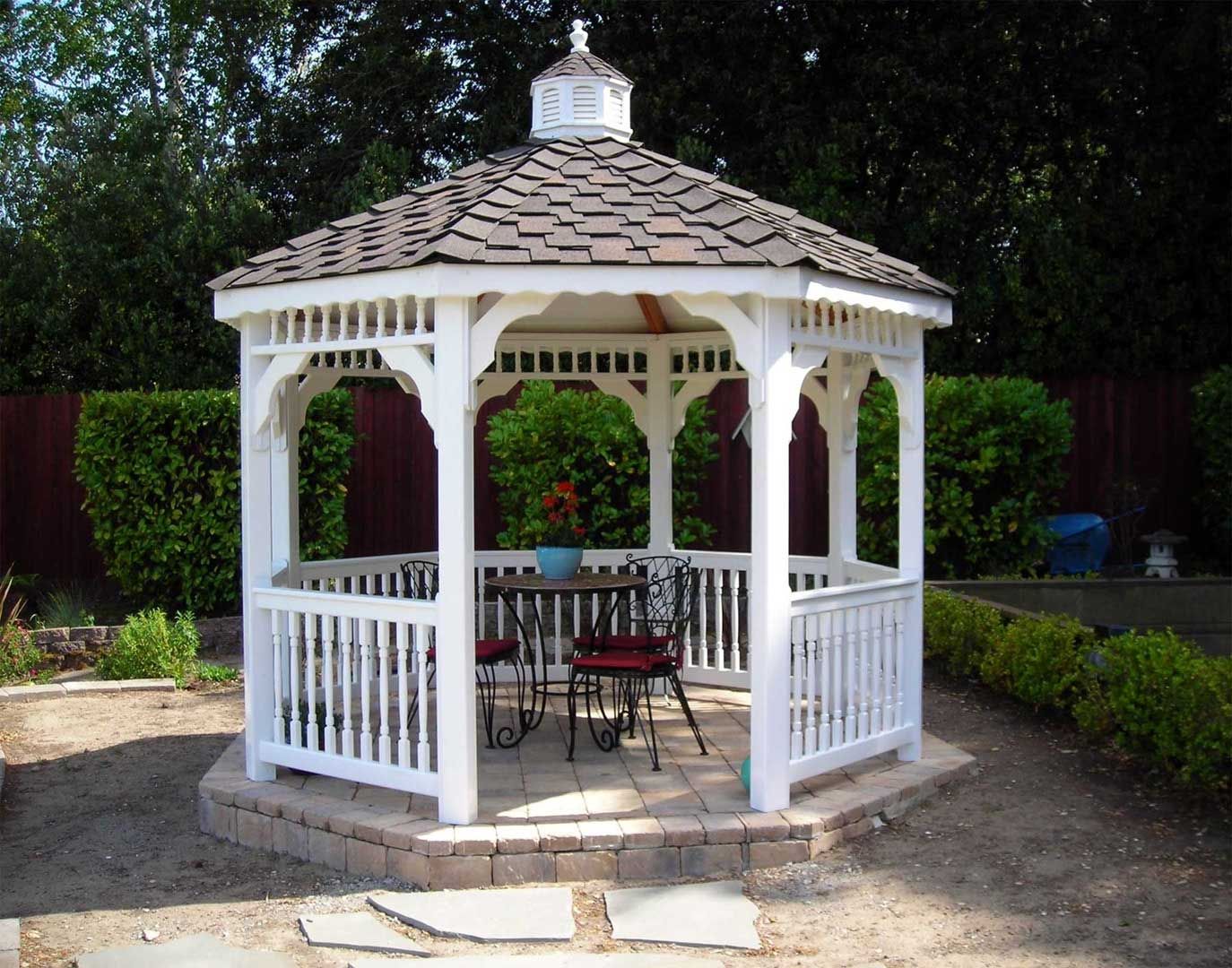 White gazebo with brown roof, outdoor setting, table and chairs inside.