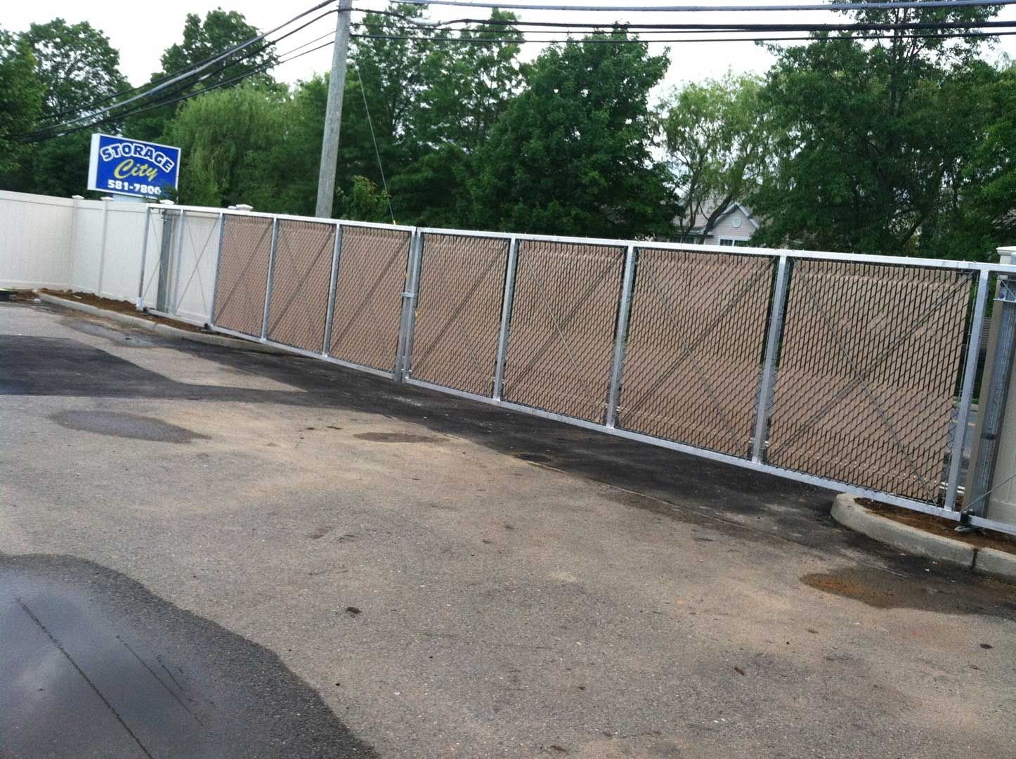 Metal fence sections with woven brown material, bordering a parking area.