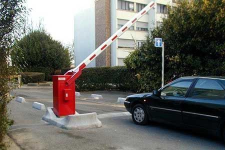 Red and white parking barrier arm raised above a black car, next to a building.