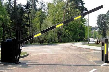 Black security gate, arm raised, across an asphalt driveway entrance with reflective yellow stripes.