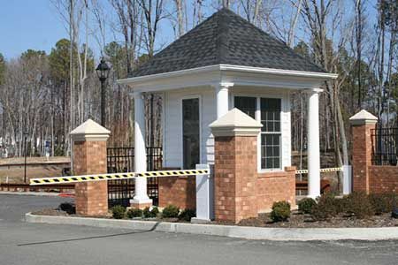 Guardhouse with brick pillars and a gate, in front of a residential community entrance.