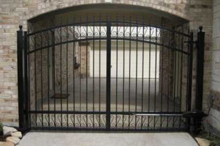 Black wrought iron driveway gate within a brick archway.