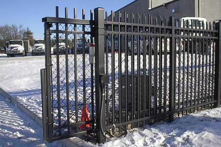 Black metal security gate in snow; a parked truck visible.