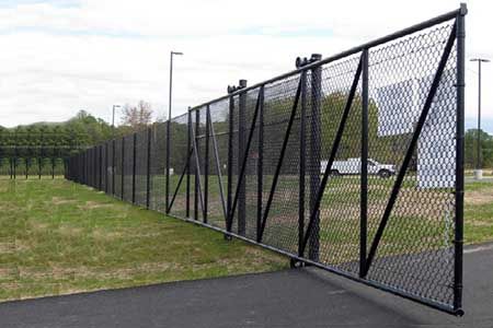 Black chain-link fence, partially open, along a grassy area and paved path. A car is visible in the background.