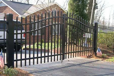 Black metal gate in front of a brick house and parked vehicle; American flags on the side.