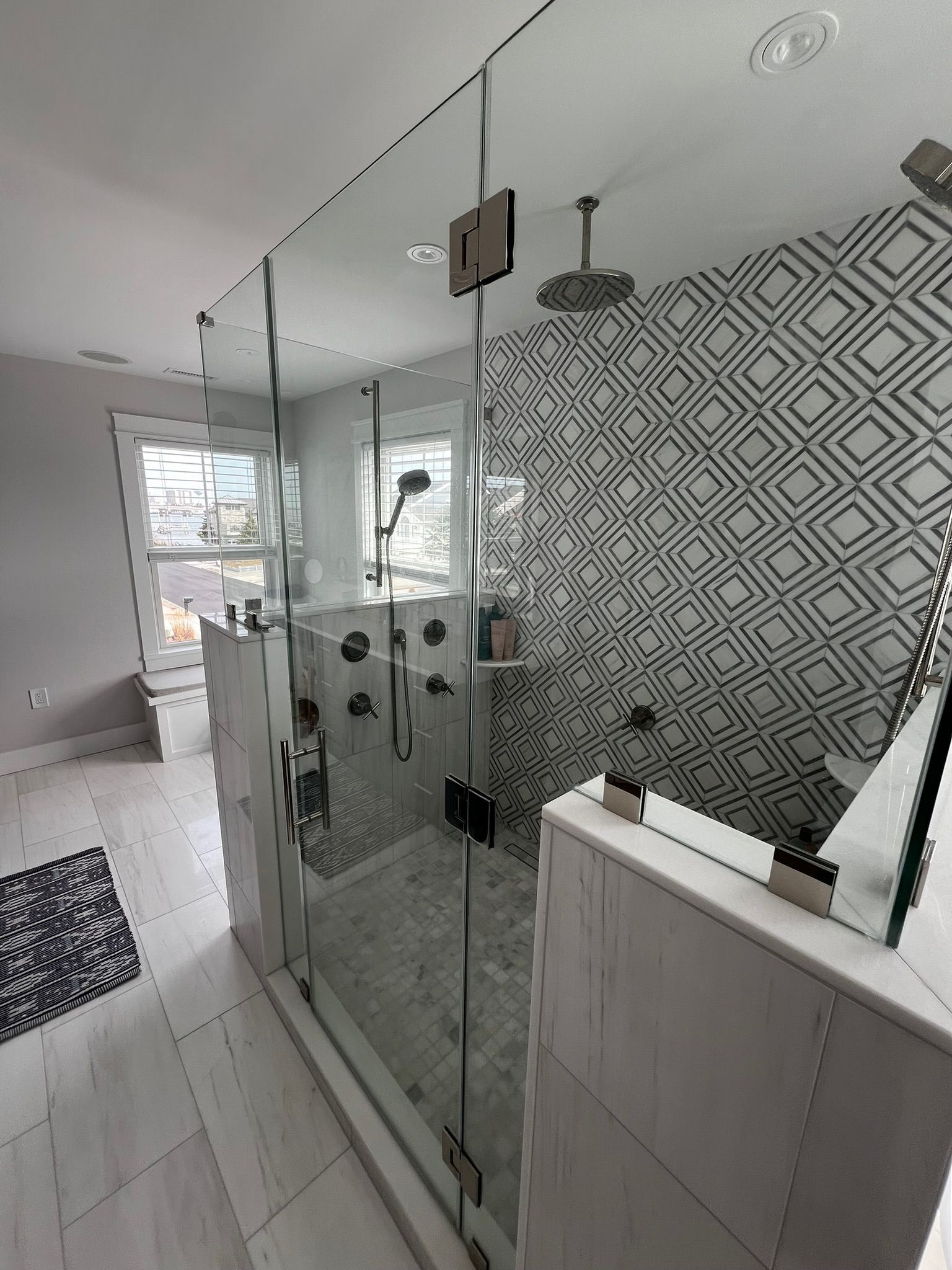 Modern bathroom with glass shower enclosure, patterned tile accent wall, and white fixtures.