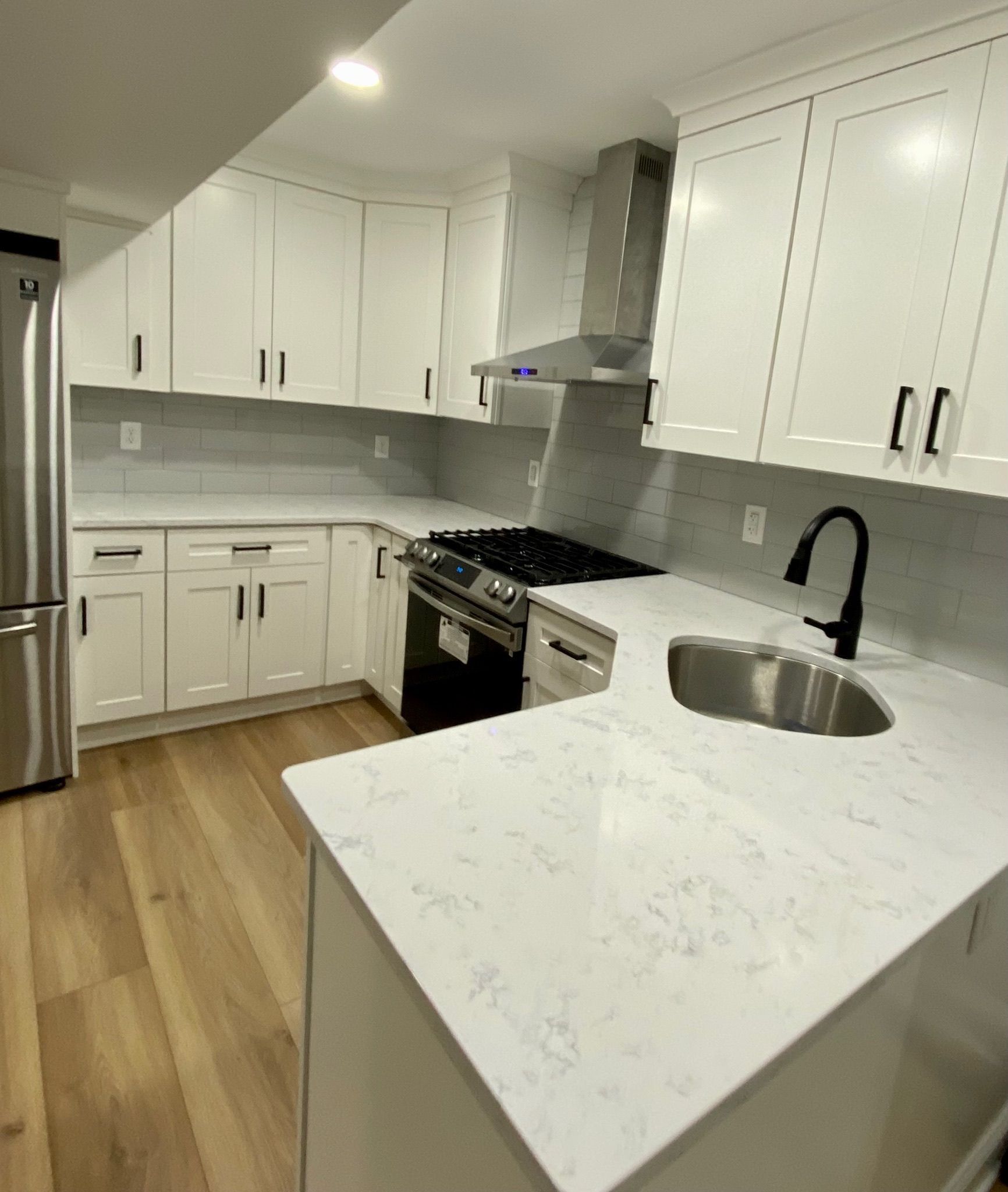 White kitchen with light countertops, stainless steel appliances, and wooden floors.