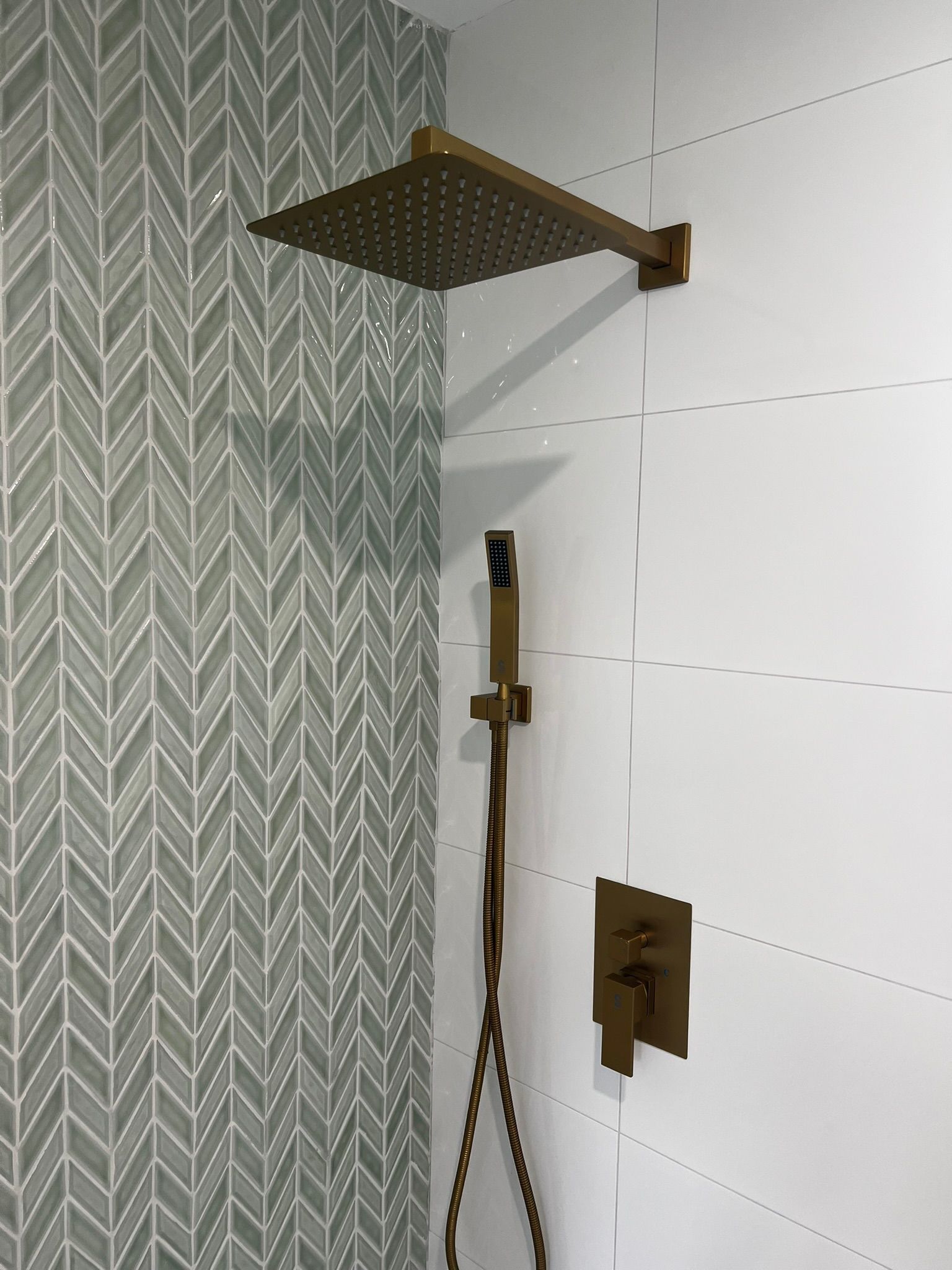 Shower with gold fixtures and patterned tile on the left wall, white paneling on the right.