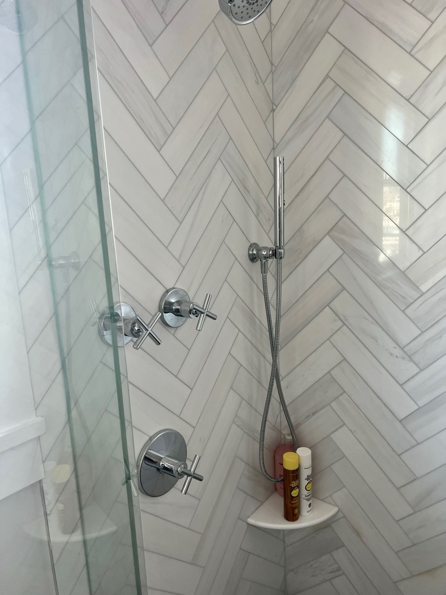 Shower with white herringbone tile, glass door, and chrome fixtures.