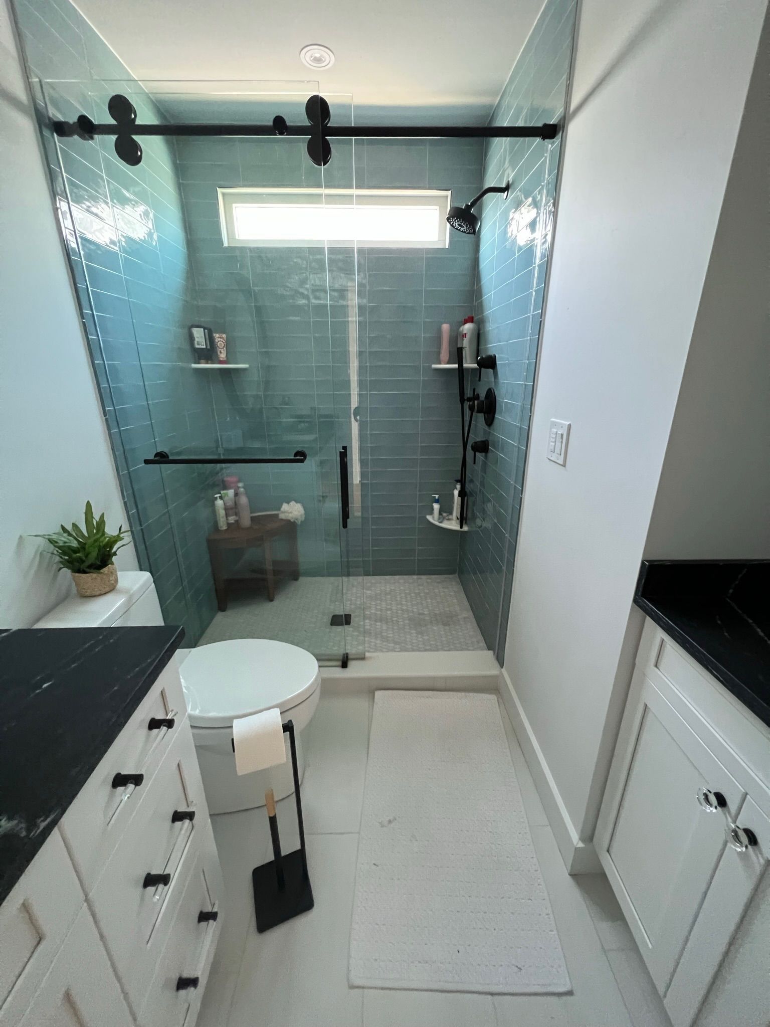 Modern bathroom with blue tile shower, glass door, white cabinets, and toilet.