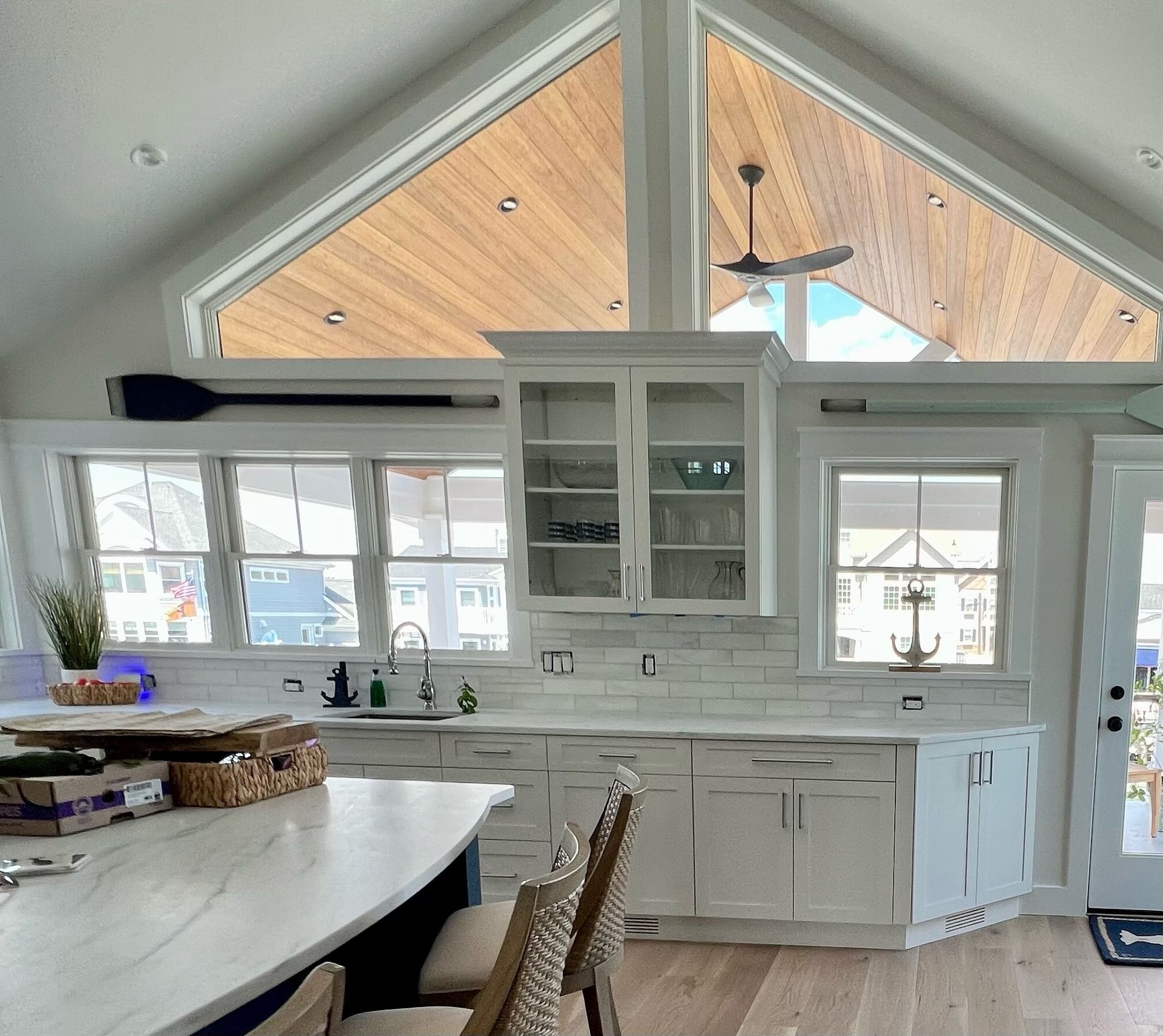 Kitchen with white cabinets, light wood ceiling, island, and large windows.