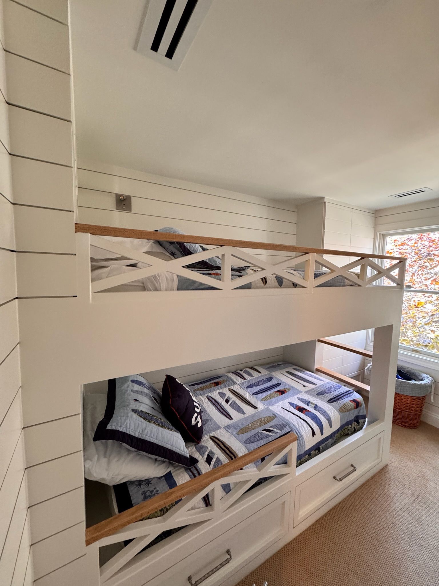 White bunk beds with wooden accents in a room with paneled walls, a window, and a woven rug.