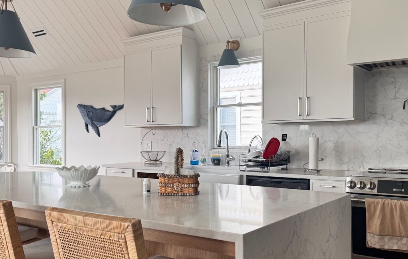 Kitchen with white cabinets, blue pendant lights, a large island, and a whale art piece.