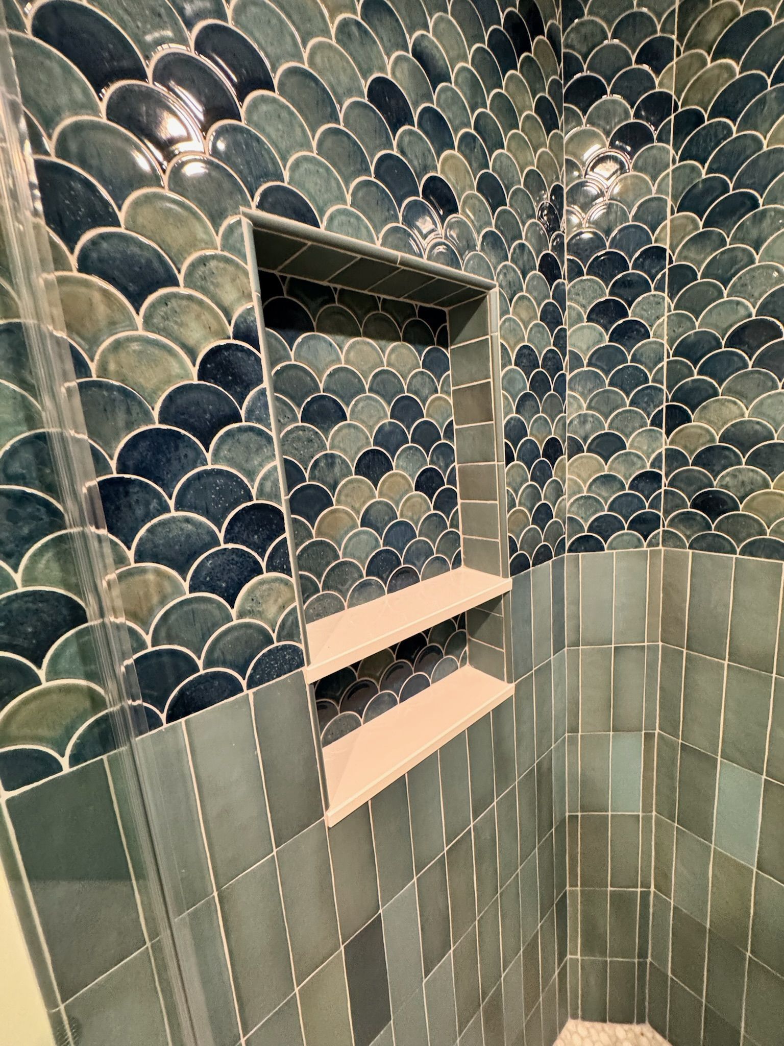 Shower with blue, fan-shaped tile above, and rectangular, blue tile below. A built-in shelf sits in the middle.