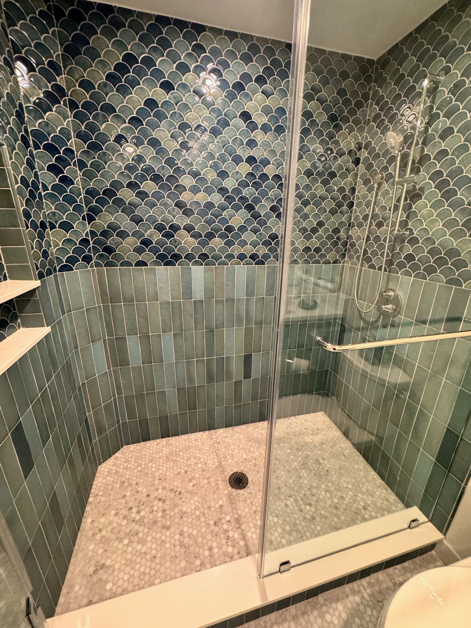 Shower with blue and grey mosaic tile walls, glass door, and water flowing.