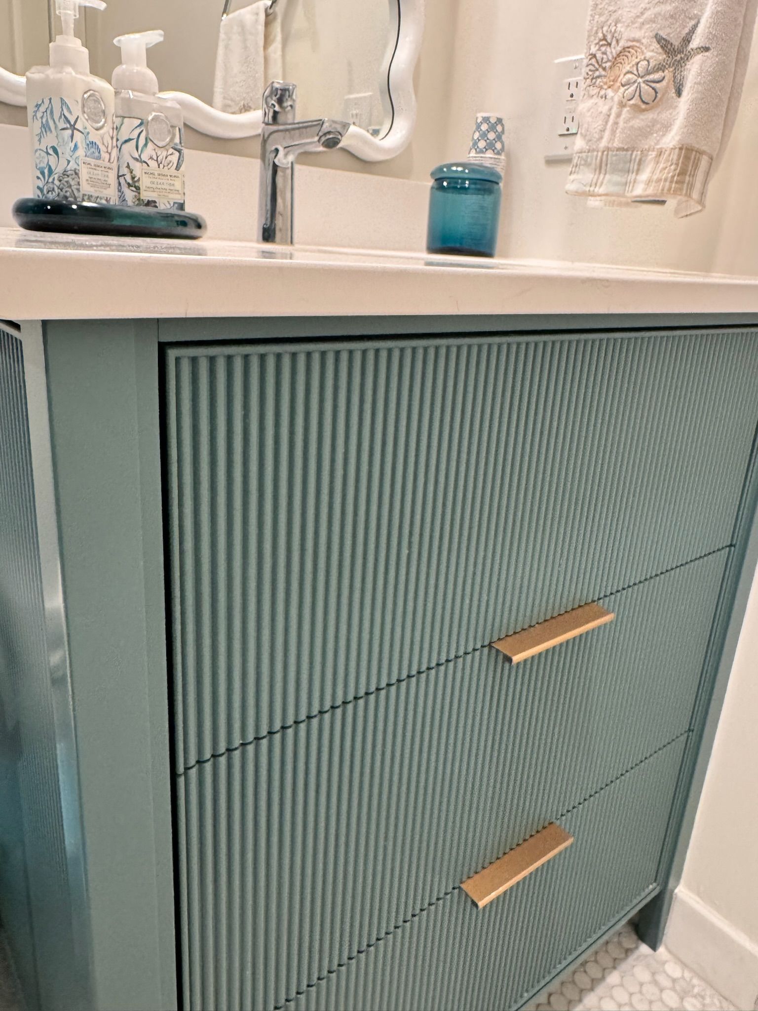 Blue bathroom vanity with ribbed drawer fronts, gold handles, and white countertop.