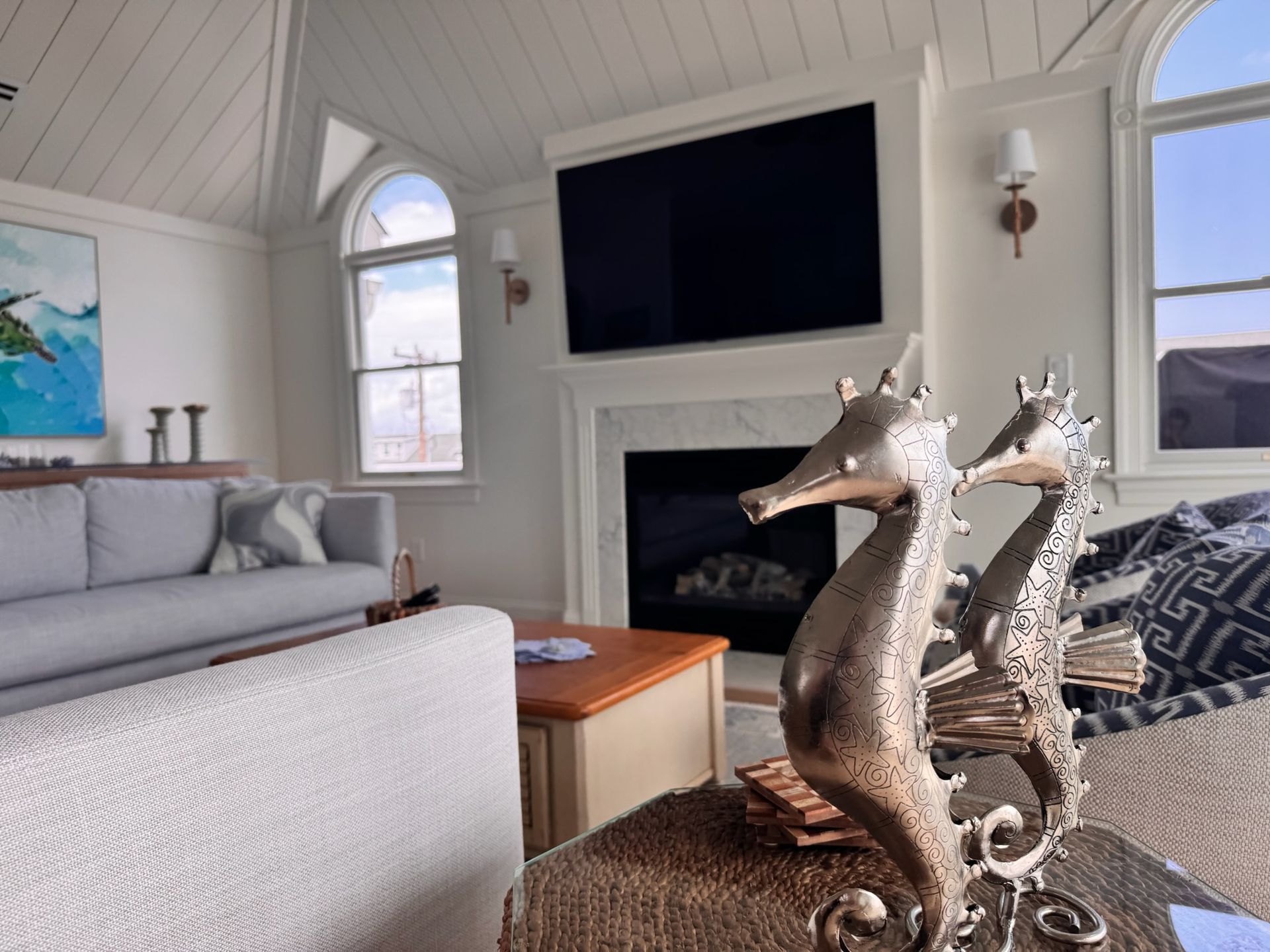 Living room with seahorse sculpture, fireplace, and arched window. Gray sofa and coffee table.
