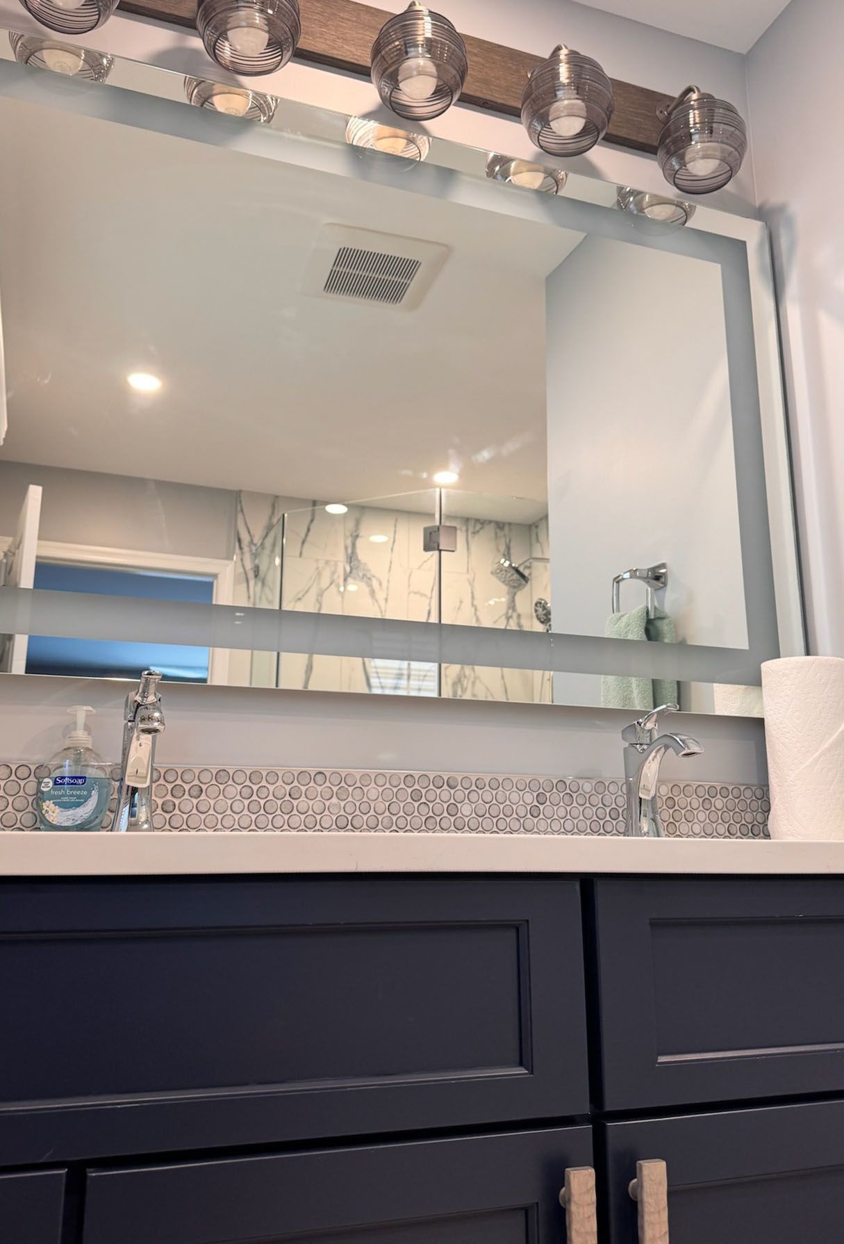 Bathroom with double sink vanity, large mirror, and decorative lighting. Blue cabinetry, white countertop.