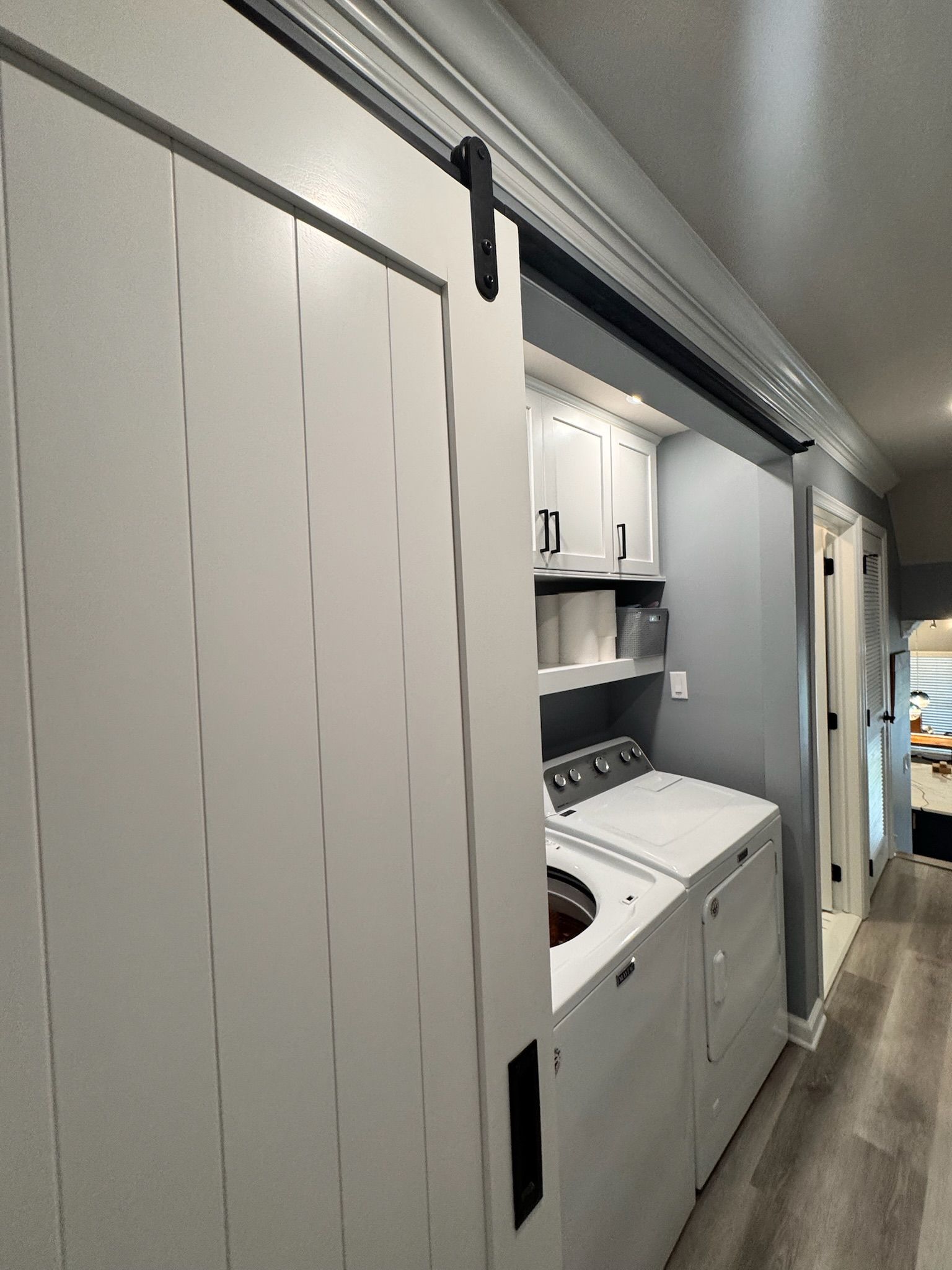 White barn door on a laundry room with washer, dryer, shelves, and cabinets.