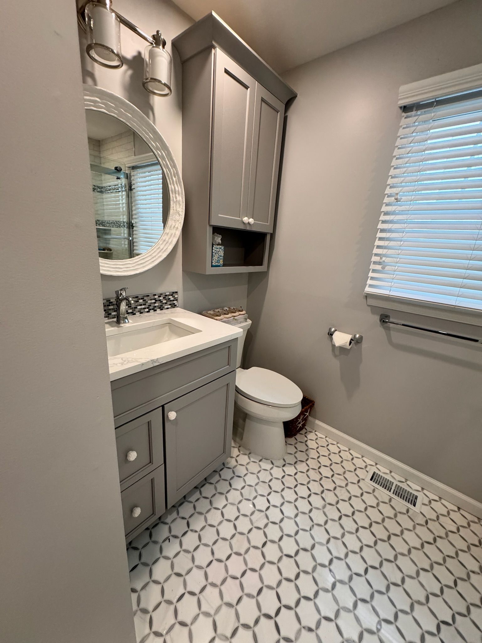 Gray and white bathroom with vanity, toilet, cabinet, and patterned tile floor.
