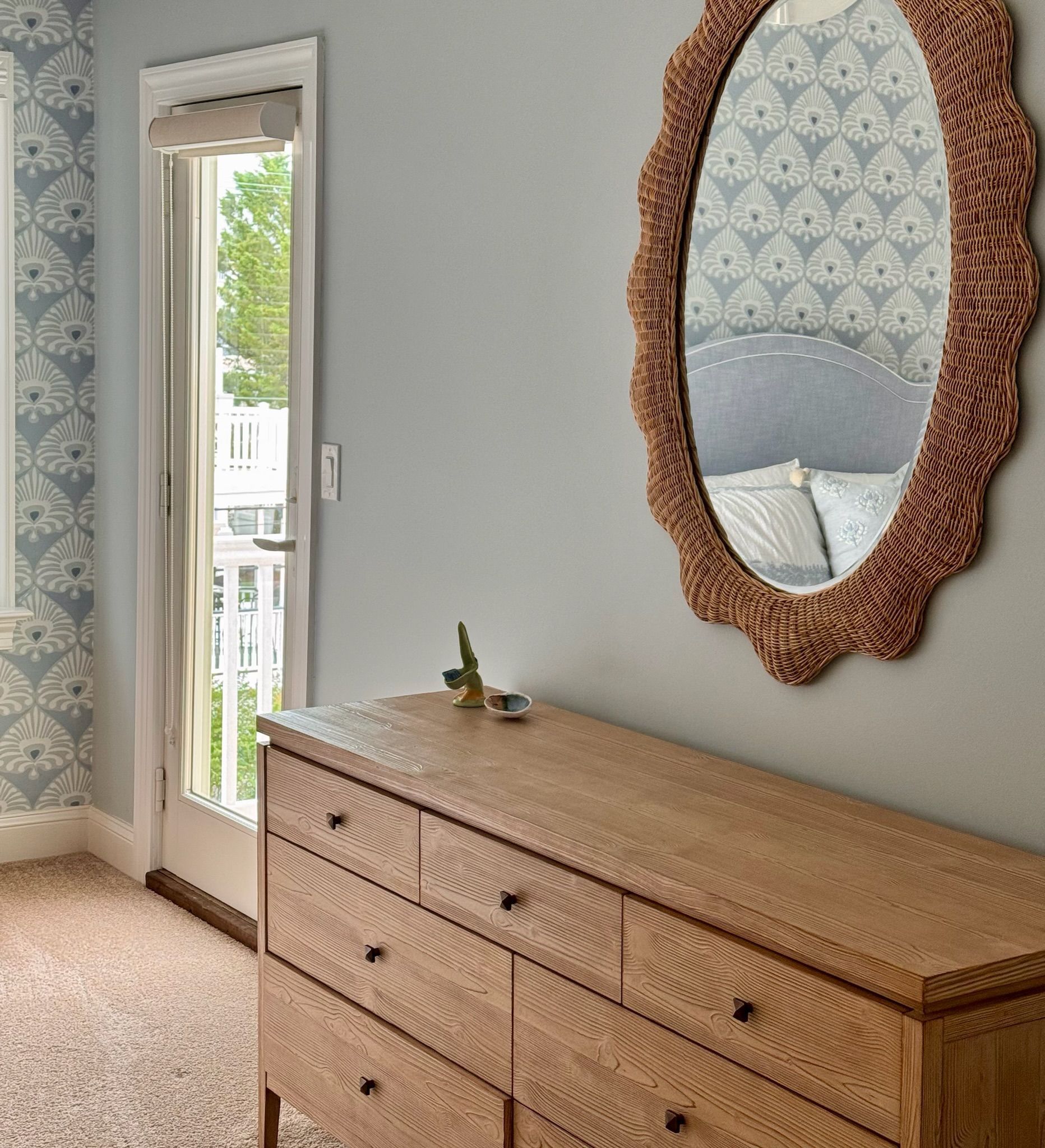 A light wood dresser with a decorative mirror above it, next to a doorway, and wallpapered wall.