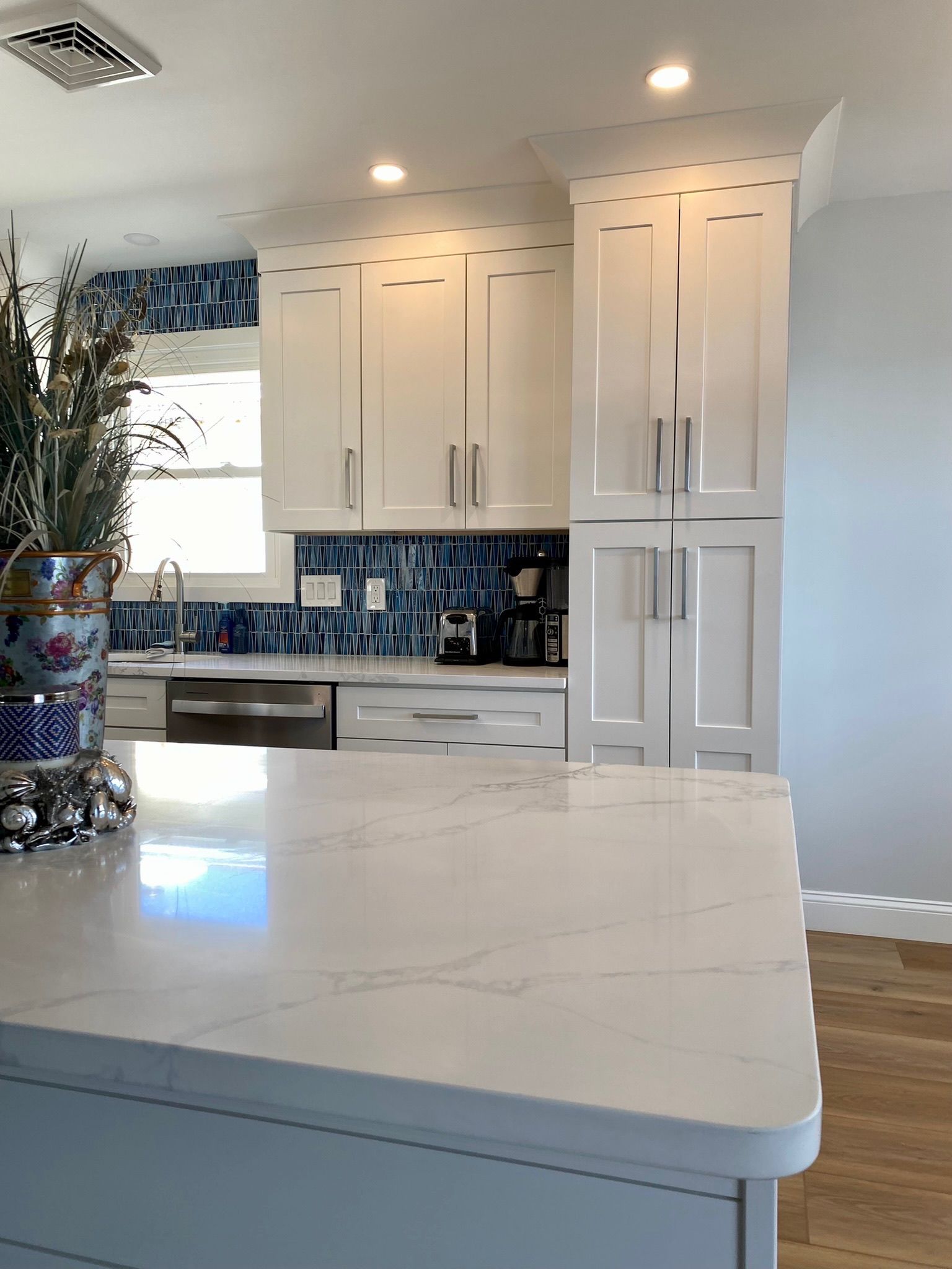 White kitchen with blue tiled backsplash, white cabinets, and quartz countertops.