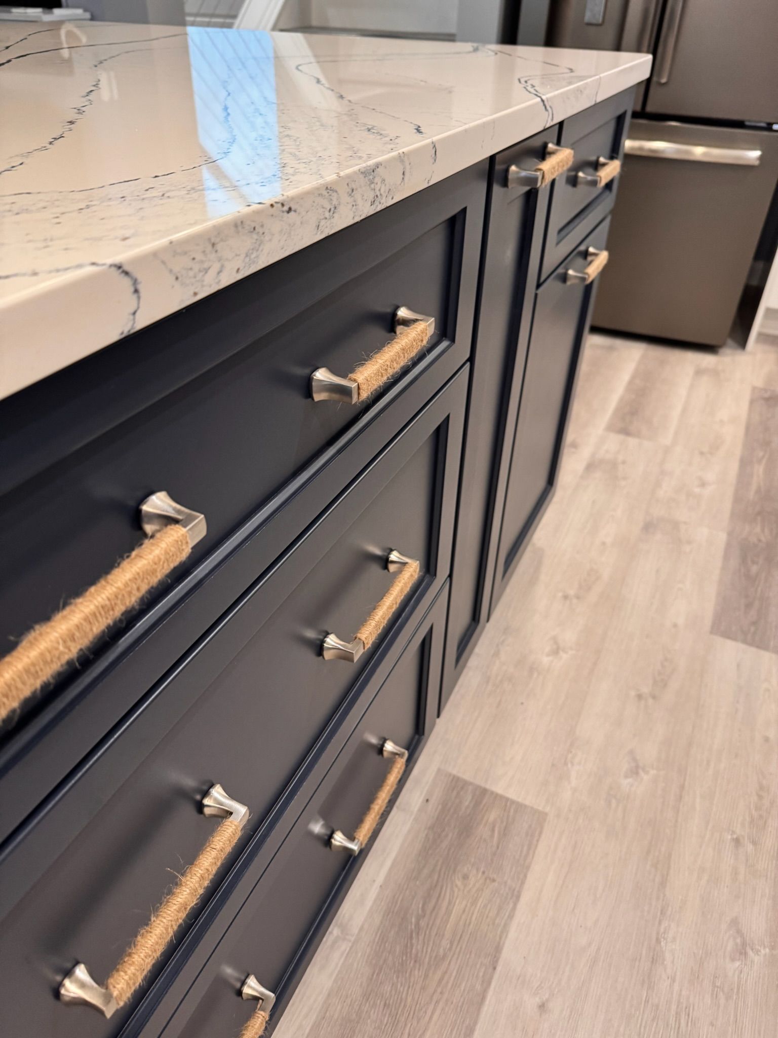 Dark blue kitchen island with a white countertop and rope-style drawer pulls.