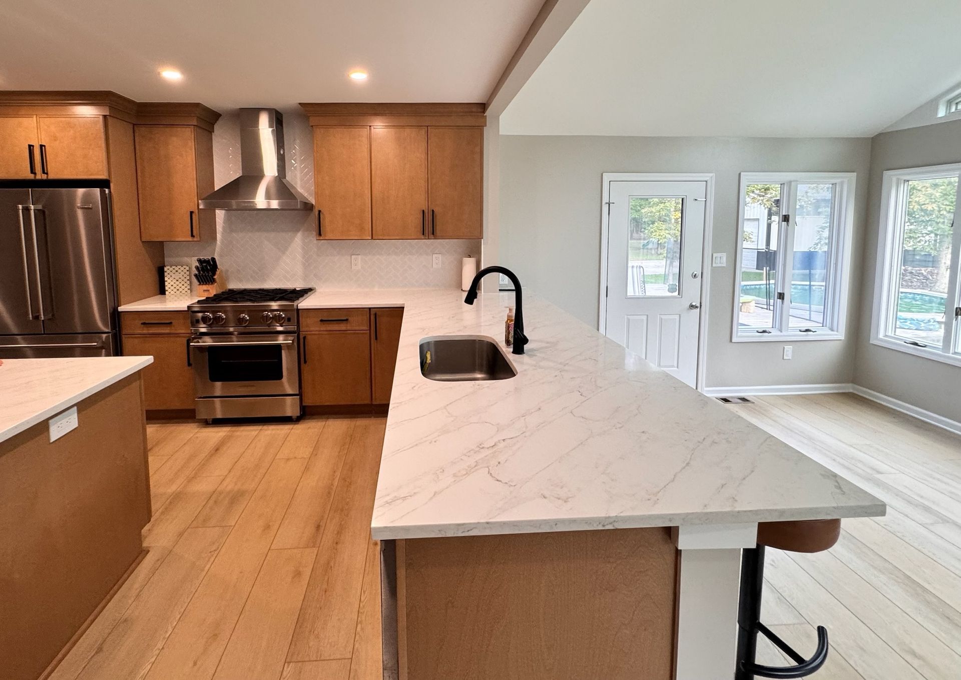 Modern kitchen with light wood cabinets, stainless steel appliances, and white countertops.