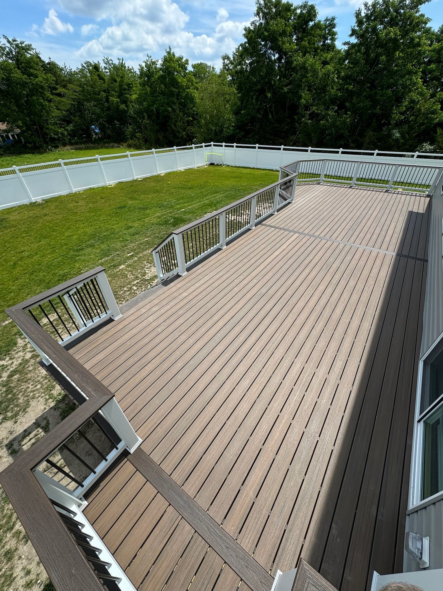 View of a brown deck with intricate cut-outs, white railing, and a grassy area with a white fence.