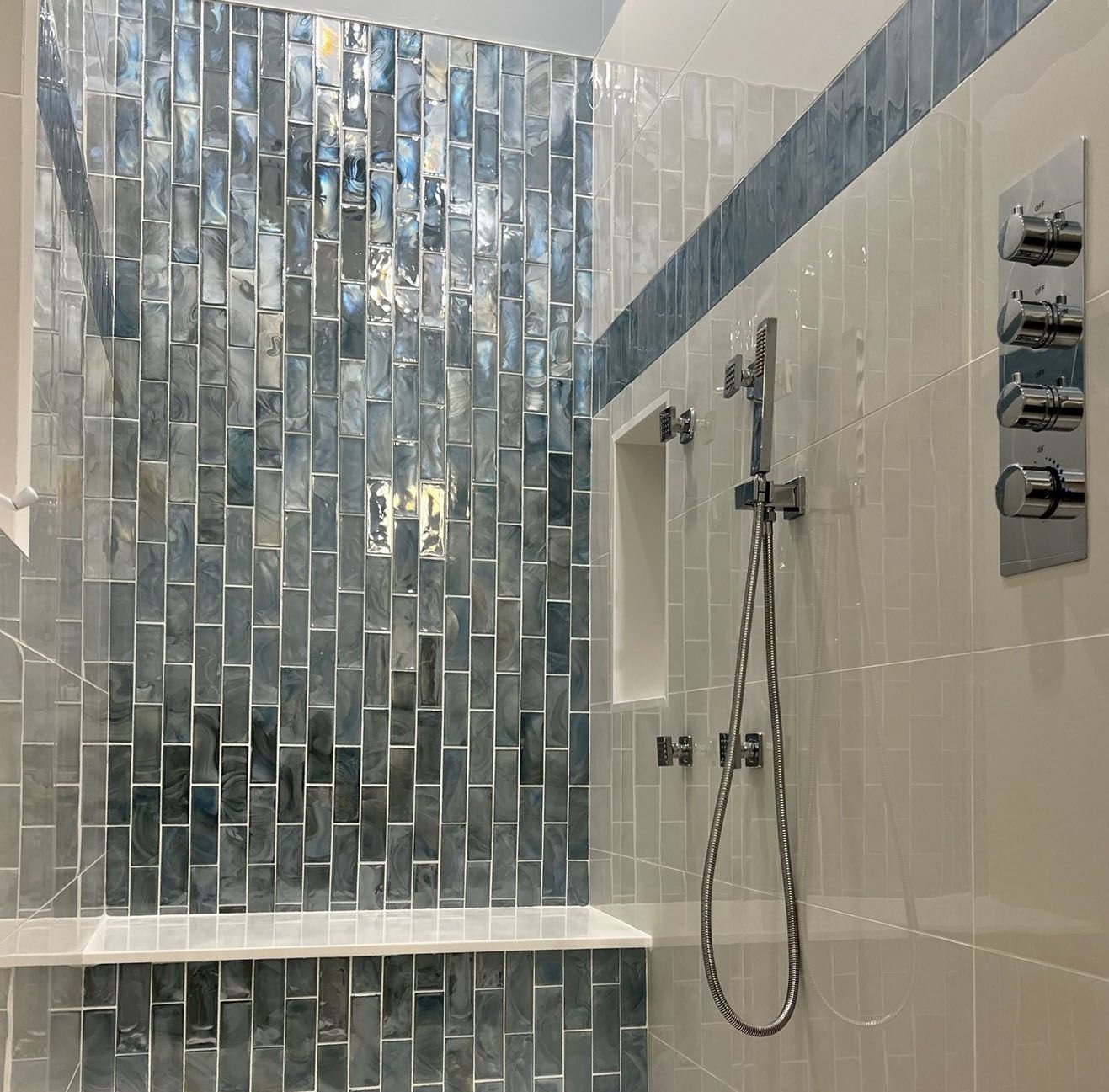 Shower with blue and silver mosaic tile accent wall, white tile, shower bench, and fixtures.