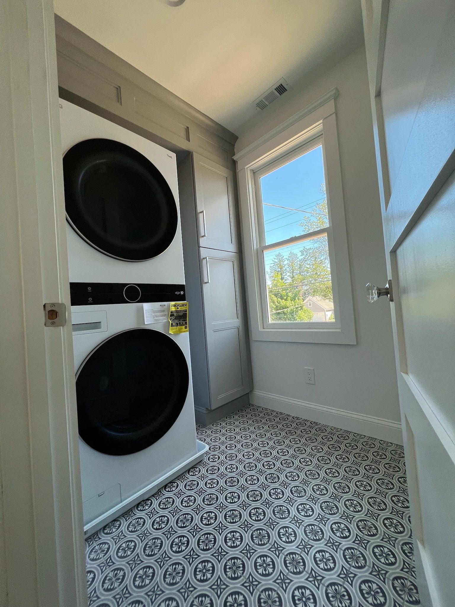 Laundry room with stacked washer and dryer, patterned floor, and a window.
