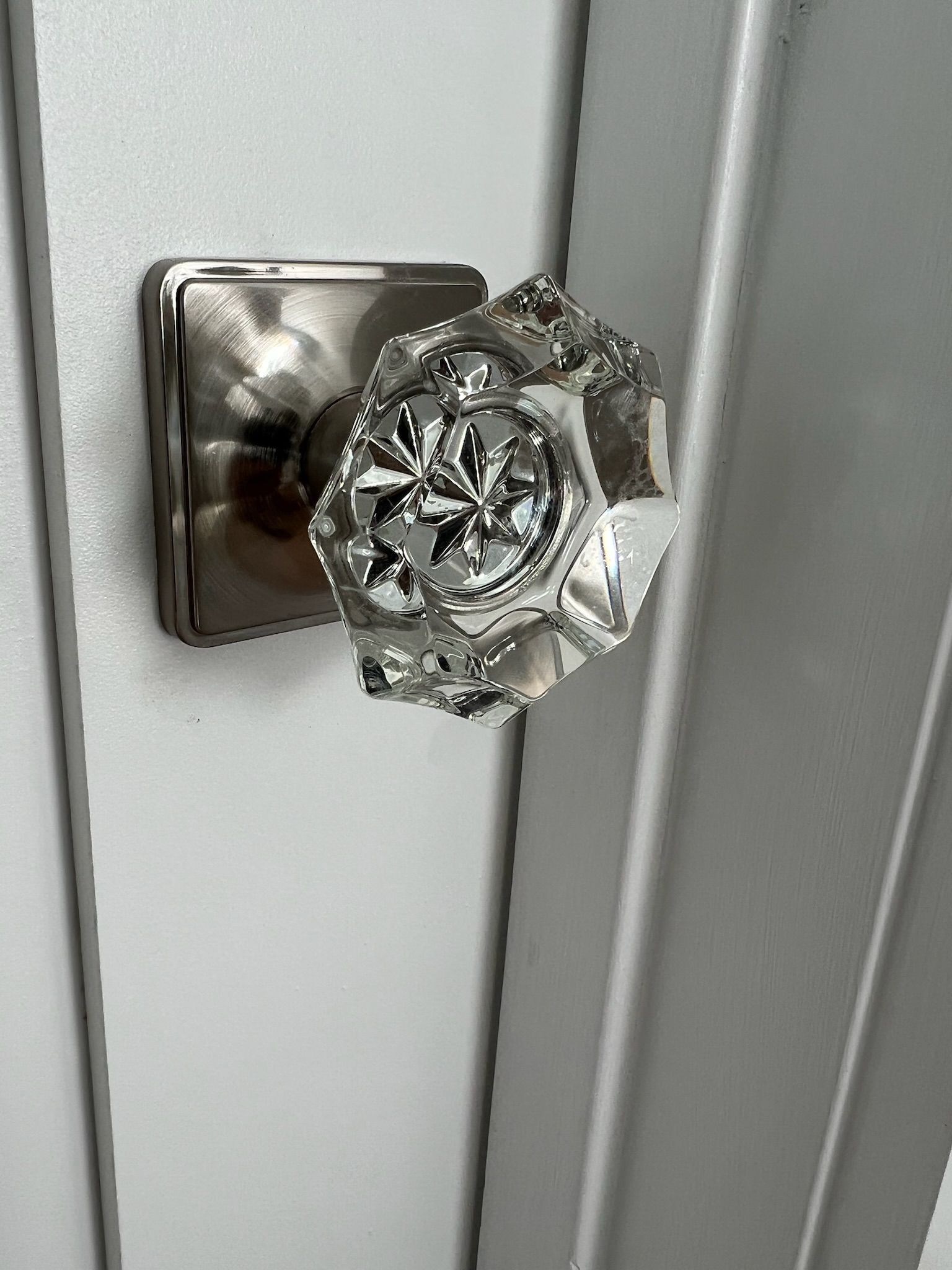 Crystal doorknob with square brushed nickel backplate on white door.