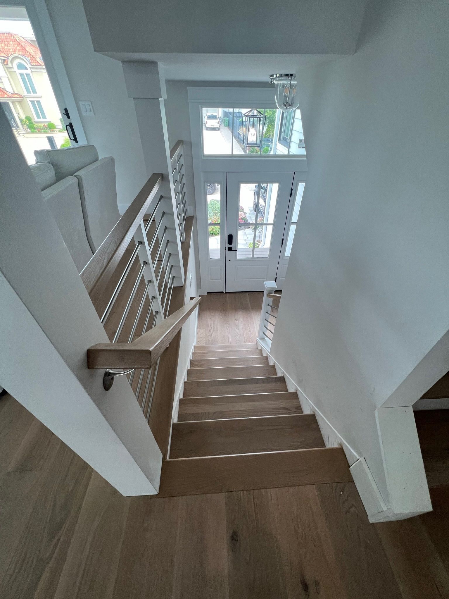 Staircase leading down to a front door. White railings and trim, wooden steps and floors. Bright, natural light.