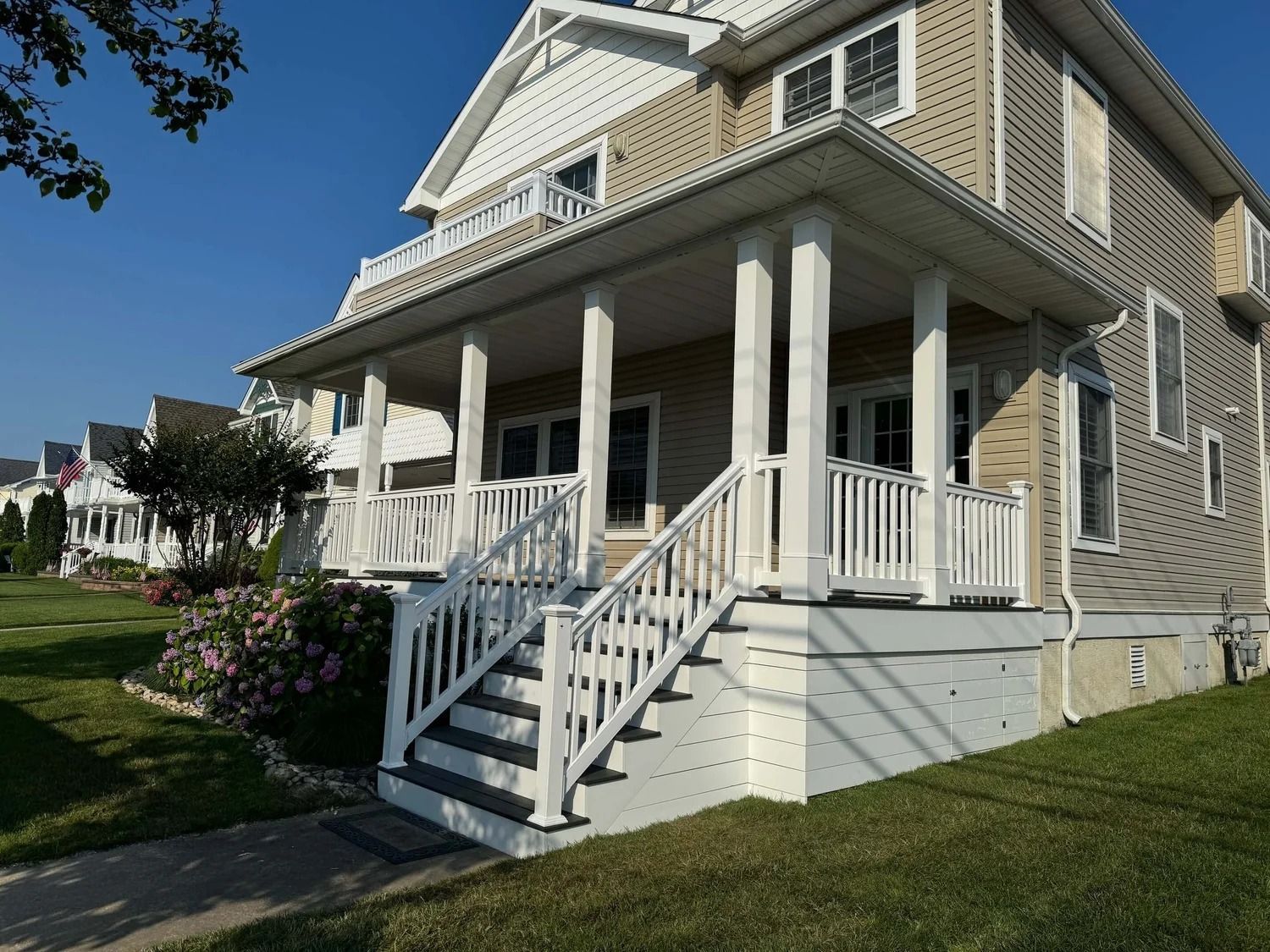White porch with steps, beige and white house, green lawn, clear sunny day.