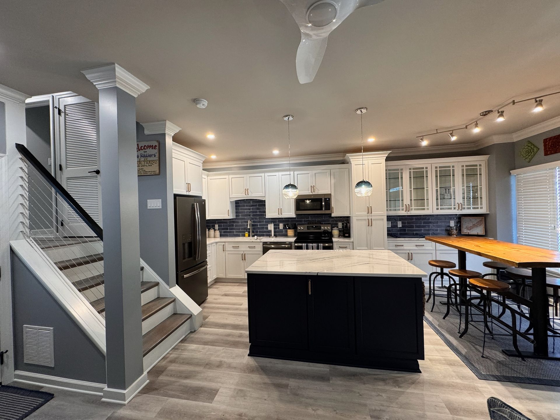 Open-concept kitchen with white cabinets, navy island, and stairs to the left.
