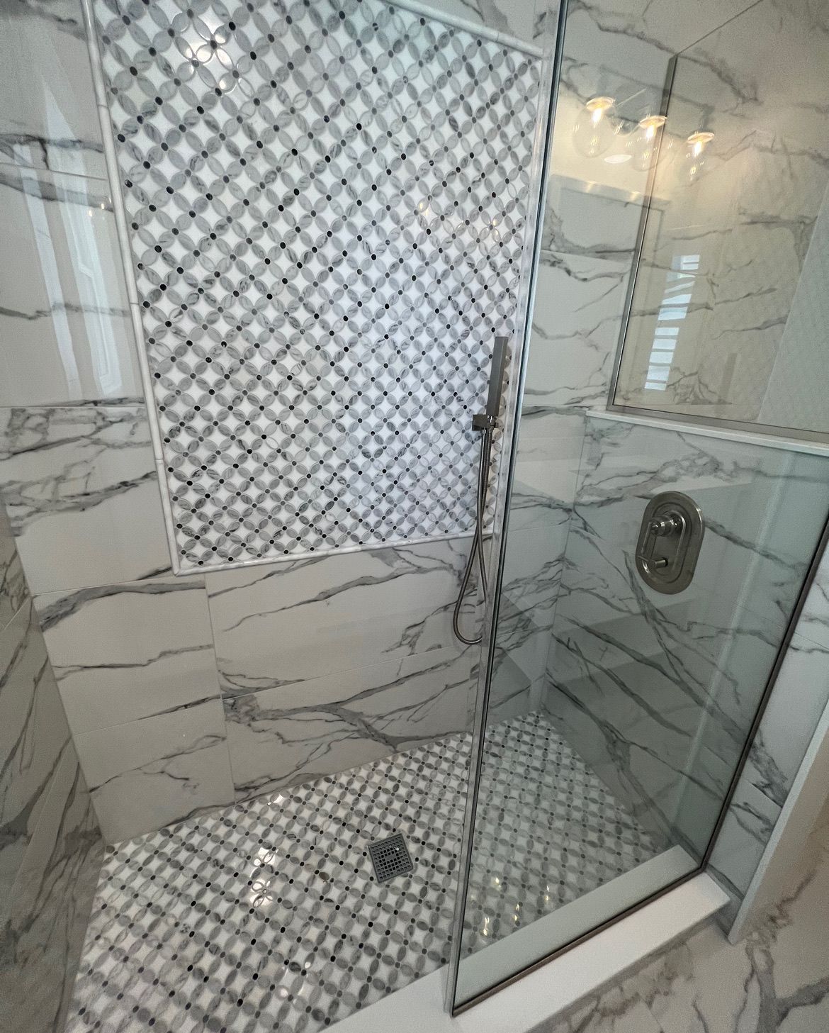 A glass-enclosed shower with white marble-patterned tiles and a diamond-patterned tile accent wall and floor.
